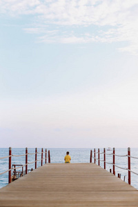 一个男孩坐在码头上, 看着海的地平线和蓝天。在海上度假。夏季时间海洋度假背景
