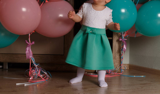 小女孩在地板上的房间旁边的气球第一个生日庆祝。 一岁的蓝色和粉红色的蝴蝶球。 穿着白色和蓝色衣服的女孩