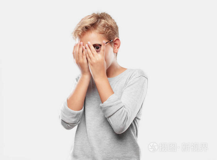 年轻的金发帅哥一个害怕的表情用双手偷看遮住眼睛