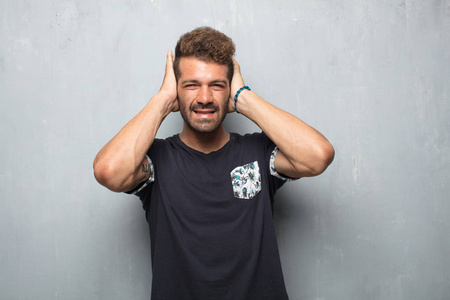 年轻的英俊男子双手捂住耳朵,以保护他们免受不舒服的大声烦人的噪音.