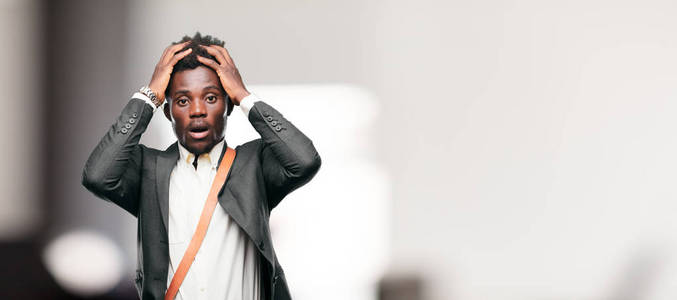 年轻的黑人商人用一种疯狂的惊讶的表情大喊大叫,双手抱着头.照片