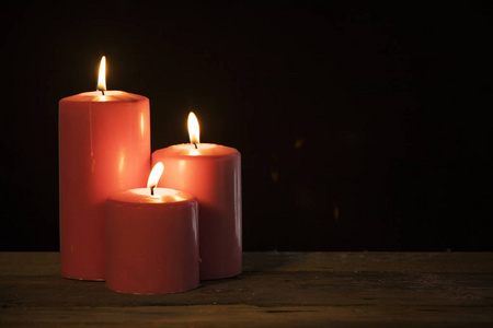 三支蜡烛在黑背景的木桌上发光的图像