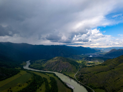 从空中俯瞰阿尔泰山的自然景观，在一场暴风雨即将来临的时候，乌云密布，一条绿色蜿蜒的河流照亮了山脚下的村庄