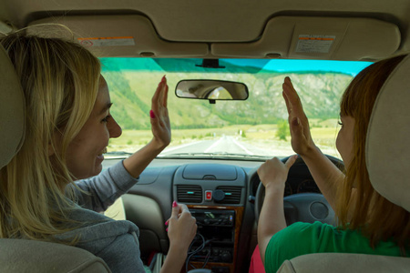 在阿尔泰山区开车旅行的两个年轻漂亮的女孩很高兴,她们笑着伸出五个