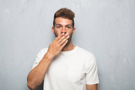 年轻的帅哥用手捂住嘴,用一种惊讶的姿势,以便保持沉默和保守秘密.