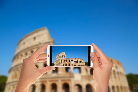 一位游客正在用手机在意大利罗马的蓝天上拍一张古罗马竞技场的照片