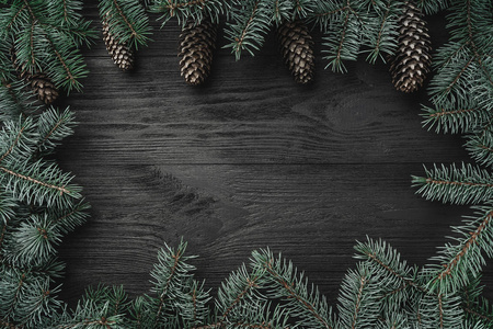 圣诞卡。 黑色木材背景，冷杉枝周围的边缘锥在顶部。 顶部视图