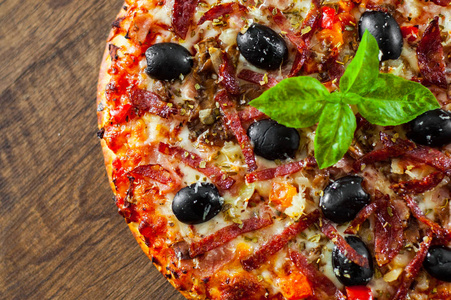披萨与莫扎雷拉奶酪，萨拉米，胡椒，火腿，意大利香肠，橄榄，香料和新鲜罗勒。 木制背景意大利披萨