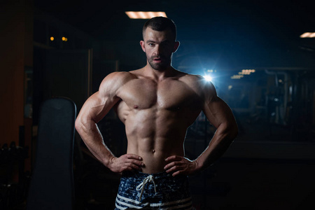 一个肌肉发达的野蛮运动员在健身房里摆姿势，炫耀他的肌肉。健康生活方式的概念