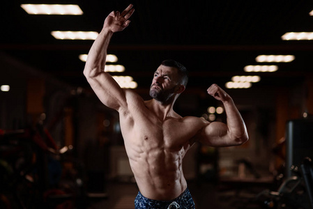 一个肌肉发达的野蛮运动员在健身房里摆姿势，炫耀他的二头肌。健康生活方式的概念