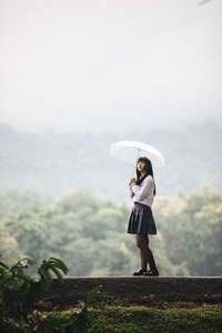 亚洲女孩的肖像，带着雨伞在雨中的自然人行道上散步