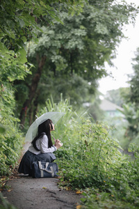 亚洲女孩的肖像，带着雨伞在雨中的自然人行道上散步