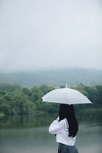 亚洲女孩的肖像，带着雨伞在雨中的自然人行道上散步