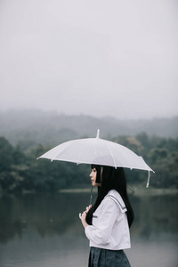 亚洲学校女孩的肖像，带着雨伞在雨中看