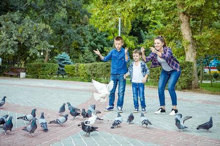 年轻漂亮的母亲和她的两个儿子一起享受喂养鸽子的乐趣。 幸福的家庭。 积极的人类情绪，感受快乐。