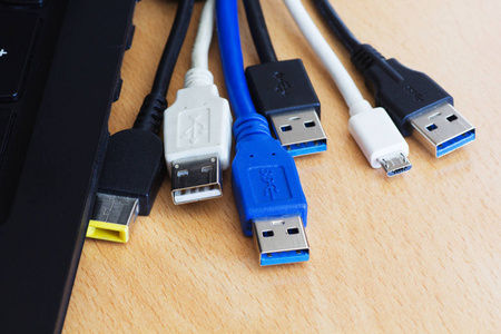 木制背景上的许多不同的USB电缆和笔记本电脑。