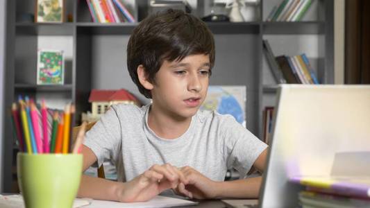 在线学习的概念。这个孩子在一所在线学校就读。男孩做家庭作业与笔记本电脑