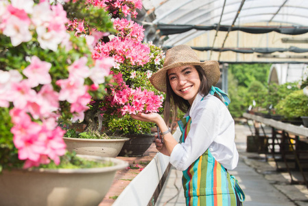 美丽的女园丁在她的花草中照顾植物，在一个温室里工作的亚洲