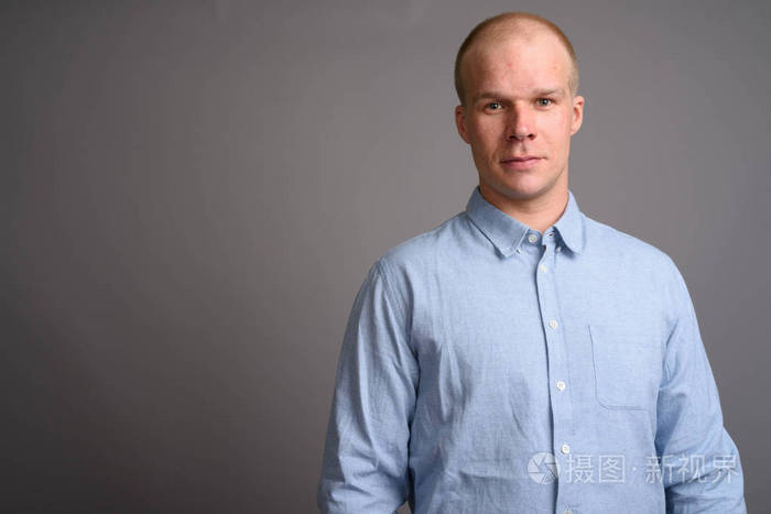 光头商人穿着蓝色衬衫反对灰色背景