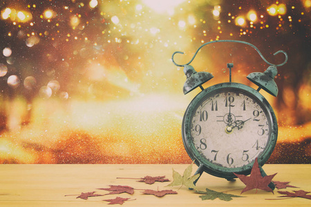 秋天时间变化的形象. 倒退概念. 乡村木桌上的干叶和老式闹钟照片