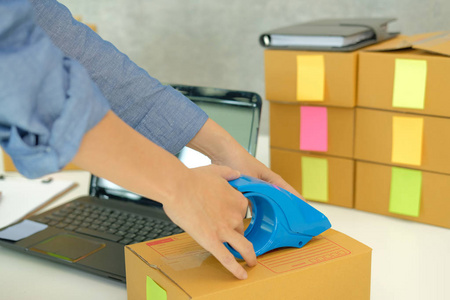 创业小企业主在工作场所包装纸板箱。 自由职业女性企业家卖家准备包裹盒的产品交付给客户。 网上销售电子商务概念