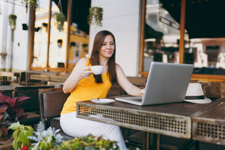平静的女人在户外街头咖啡厅，坐在桌子上，工作在现代笔记本电脑，电脑，喝杯茶，在餐厅放松，在空闲时间。 移动办公自由职业概念