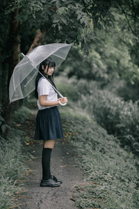 亚洲女孩的肖像，带着雨伞在雨中的自然人行道上散步