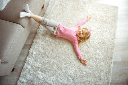 愉快的小女孩躺在地板上的沙发附近