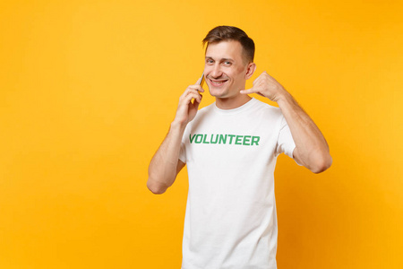 一幅年轻人的画像，白色T恤，上面写着绿色的标题，志愿者在黄色背景下用手机聊天。自愿无偿援助，慈善恩典工作理念