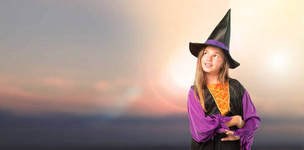 穿着女巫的小女孩在万圣节假期站起来，仰望户外日落
