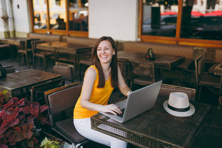 妇女在户外街头咖啡厅，坐在桌子上，工作在现代笔记本电脑电脑，在餐厅放松，在空闲时间。 夏天的移动办公室。 生活方式自由职业商业概