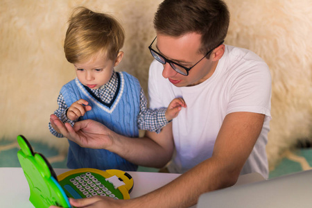 年轻英俊的父亲和他可爱的小儿子在室内玩玩具笔记本电脑