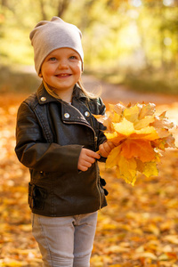 小女孩穿着皮夹克，在秋天的公园里玩。