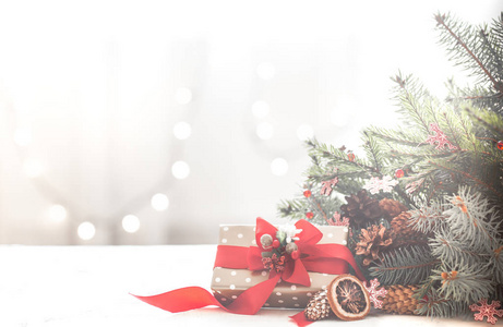 在一个灯光背景的房间里，圣诞舒适，有灯光和圣诞树的树枝，桌子上有一个红色蝴蝶结的礼物，有文字的空间