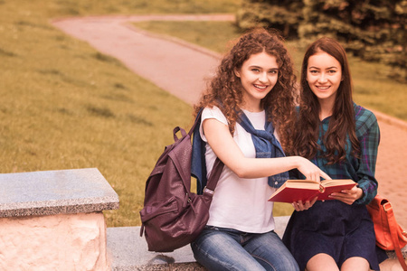 两个年轻的快乐女学生坐在户外，手里拿着书