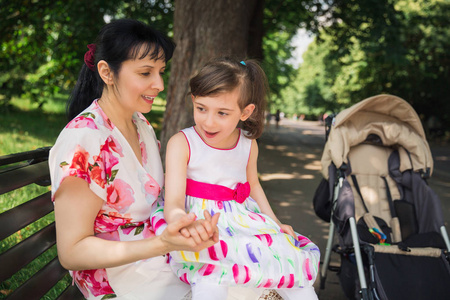 年轻快乐的母亲坐在长凳上，抱着她快乐的残疾女儿在户外散步