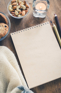 平躺空白棕色笔记本与针织毛毯和零食在木桌上。 舒适的秋天或冬天的心情。 复制空间。