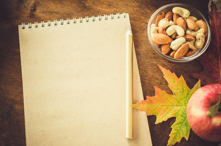 用坚果苹果和秋叶的空白棕色笔记本平躺在木桌上。秋天的静物。惬意的秋意..复制空间。