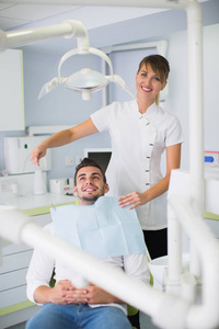 女性牙医在临床治疗前对男性患者调整围裙的图像。