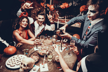 穿着服装喝香槟的年轻人。 一群穿着万圣节派对服装的年轻人坐在桌子旁喝香槟。 年轻人在喝香槟