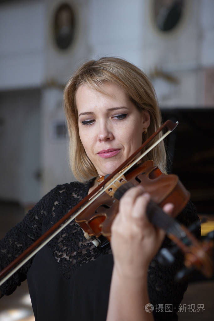 年轻漂亮的女小提琴手看着相机在她的肩膀上拿着弓特写肖像