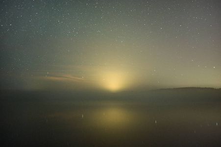 雾蒙蒙的湖面上的星空. 地平线上的城市光污染.照片