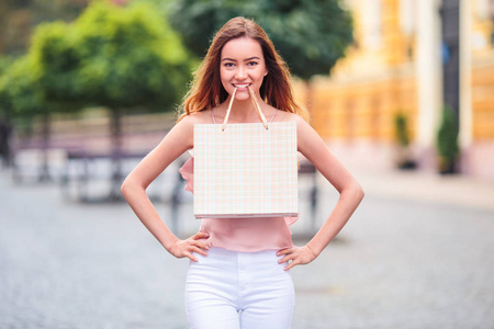 年轻可爱的女人站在街上，把购物袋戴在牙齿上