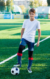 可爱的小男孩穿着白色蓝色运动服站在球场上的古典黑白足球旁边。 足球游戏训练爱好概念。