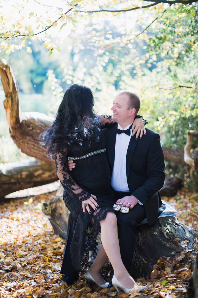 一个孕妇坐在她丈夫的腿上,她的丈夫在公园里把一双小鞋子放在她的