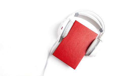 红色的书，上面有白色的耳机在白色的背景上。 有声书的概念。 顶部视图，有文本空间
