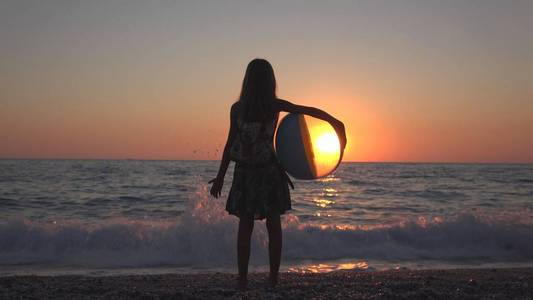 孩子在日落时玩沙滩球，孩子在看海浪，女孩在日落时看风景