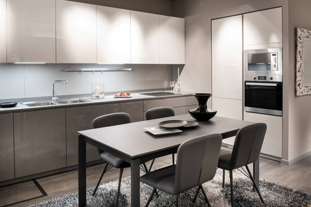 单色灰色和白色厨房内部，内置橱柜和电器，中心餐桌和椅子与花瓶