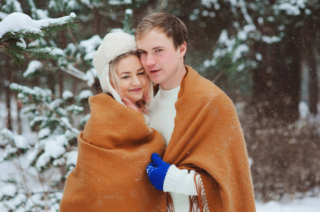 幸福的年轻情侣走在白雪皑皑的冬林里，裹着超大的围巾和拥抱。 户外活动寒假。