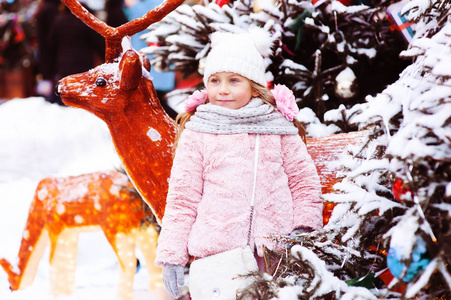 寒假的肖像，快乐的女孩走在城市，装饰圣诞节和新年摆在玩具鹿与花环和灯光附近。